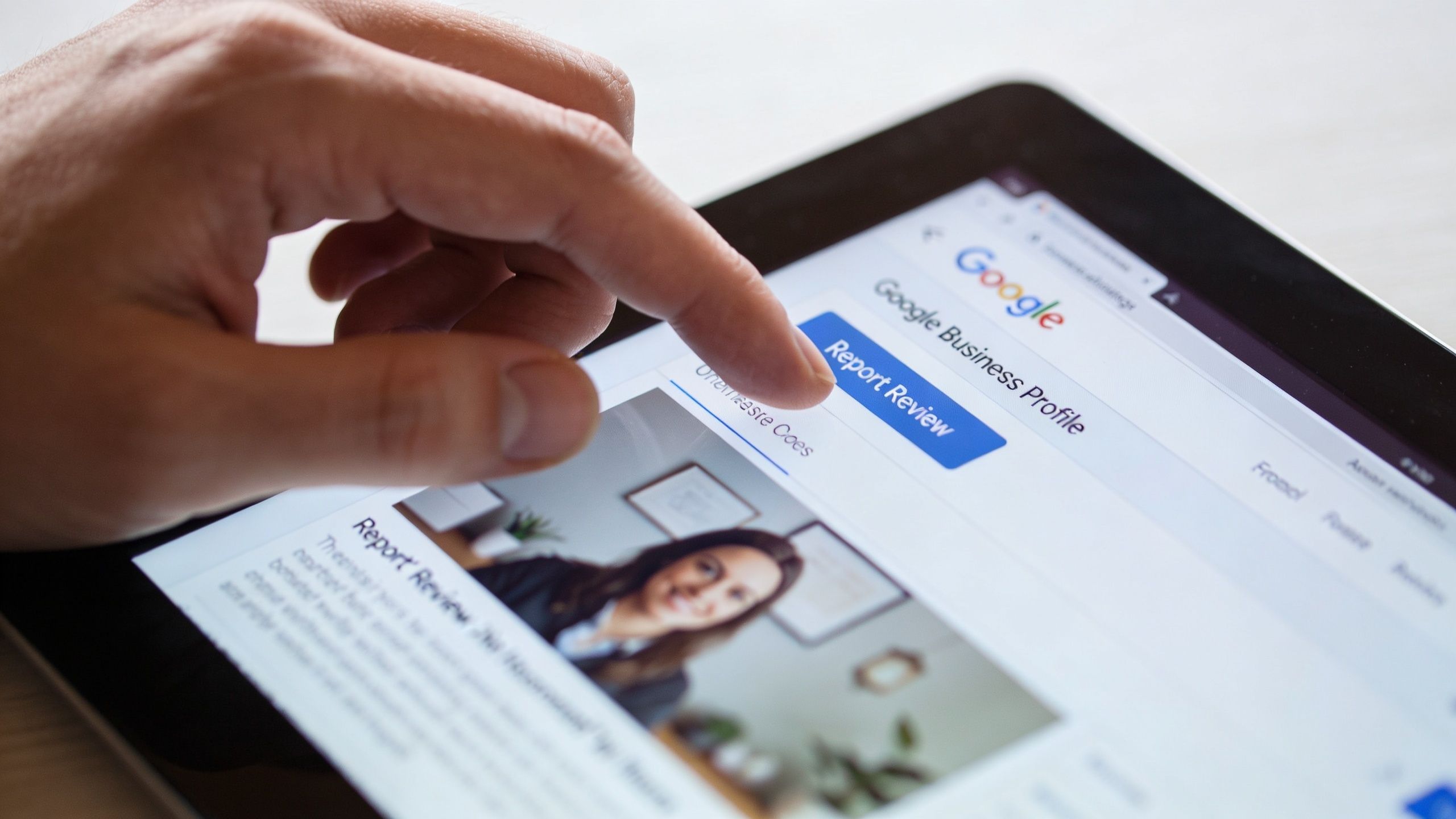 A person using a tablet to report a Google review on a business profile page.