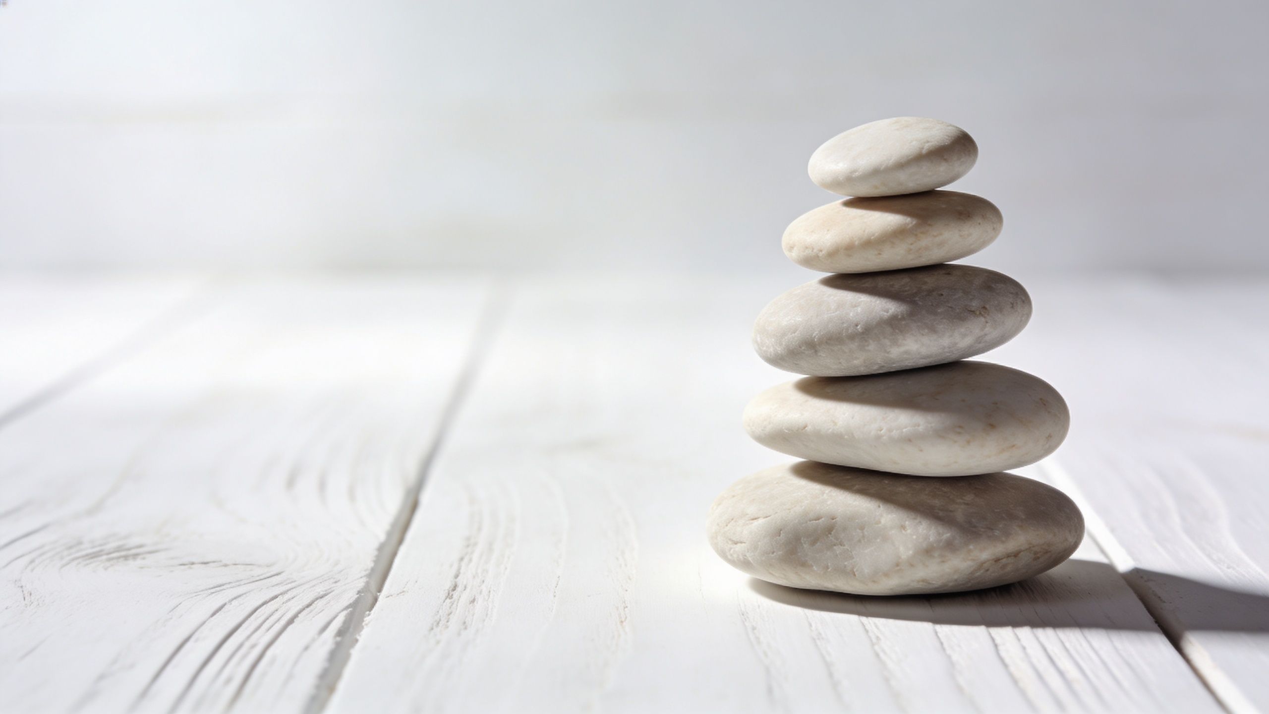 A stack of smooth, light-colored river stones balanced neatly on a white wooden table surface.